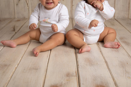 Two cute little baby girls sitting on the wooden floor and holding thermometerの写真素材