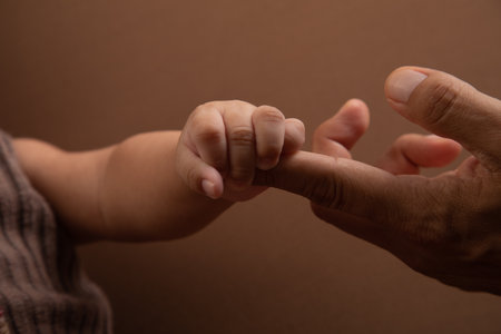 Father and son holding hands on a brown background, close-up