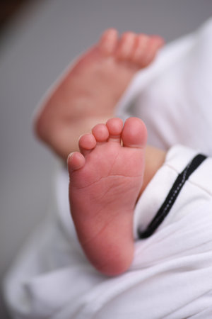 Feet of a newborn baby in a white dress on a gray backgroundの写真素材