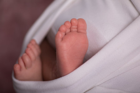 Feet of a newborn baby wrapped in a white blanket on a pink background