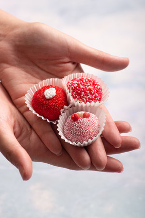 Brigadeiros Brasil Brasilianm dessert sweet food gourmet Hand holding red and white chocolate truffles on blue background.の写真素材