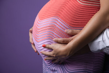 Pregnant woman with her hands on her belly against a purple backgroundの写真素材