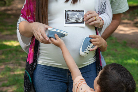 Pregnant woman and her son holding ultrasound scan in the park