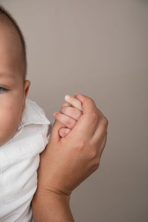 Mother holding her baby's hand. Close-up. Gray background.