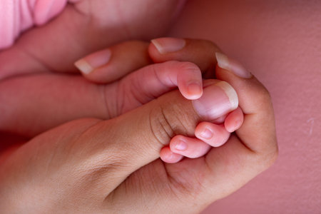 Baby's hand holding mother's hand on pink background, closeup