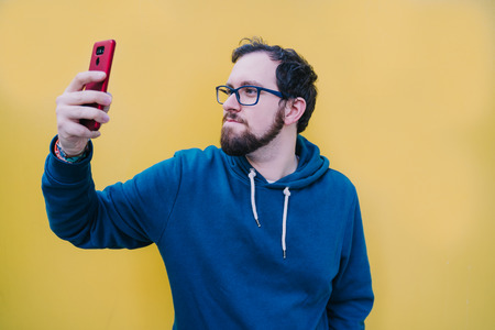Young boy is on the street in front of a yellow wall looking at something on his mobile. Lift the...