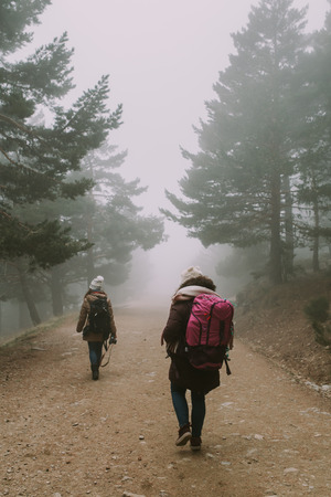 Two backpackers go down the path between trees and fogの写真素材