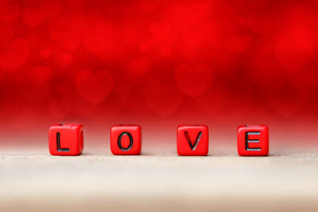 Red block cube with love word on wood table. Red blur background with heart shape. Concept of valentine dayの写真素材