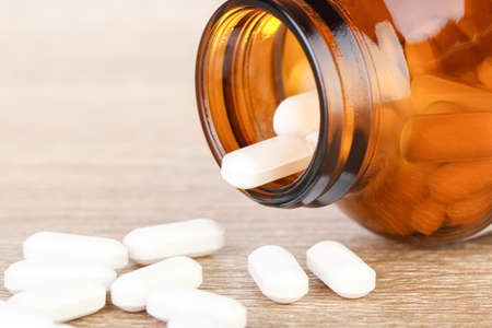 Bottle and scattered pills on brown wood backgroundの写真素材