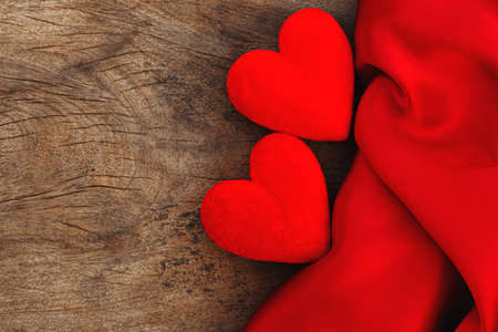Two red hearts and red satin fabric on brown wood background. Valentines day backgroundの写真素材