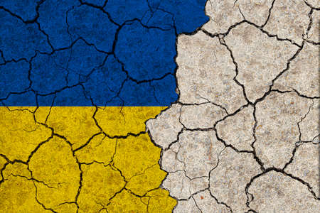 Ukraine national flags grunge pattern on grungy dry cracking parched earth. Cracked soil.の写真素材