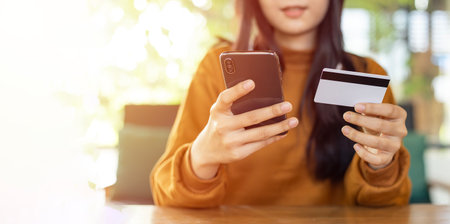 Asian woman holding smartphone and credit card  to shopping online and paying her orderの写真素材