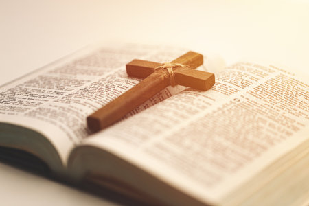 Wooden Christian cross on an open Bible with warm sunlight, symbolizing faith, hope, and spiritual devotion. Perfect for religious, worship, or inspirational themes.の写真素材