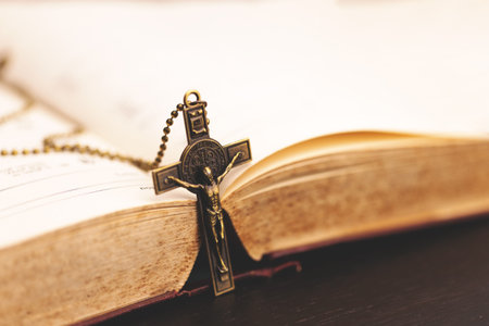 Close-up of a crucifix necklace hanging over the edge of an open Bible, symbolizing Christian faith,...