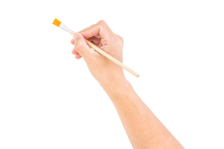 Hand holding a small flat paintbrush with wooden handle, isolated on white background, ideal for painting, art, or craft demonstration.の写真素材