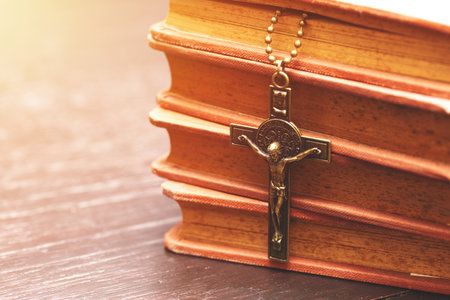 Close-up of a crucifix necklace hanging on a stack of vintage books, symbolizing Christian faith, devotion, tradition, and spiritual reflection.の写真素材