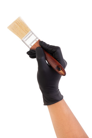 Hand wearing a black glove holding a wooden-handled paintbrush against a white background, symbolizing painting, renovation, or craftsmanship.の写真素材