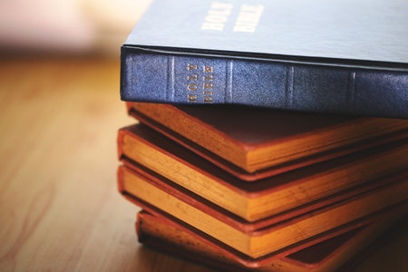 Stack of vintage Bibles with a close-up focus on the spine of a blue Holy Bible on top. Represents religious study, Christian faith, scripture preservation, and spiritual tradition.の写真素材