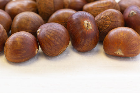 Natural brown chestnuts scattered on white rustic wood, ideal for food themes, autumn concepts, and healthy eating visuals.の写真素材