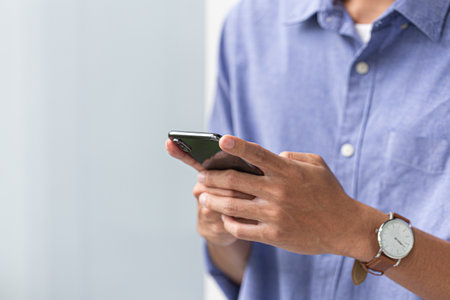 Midsection of a man in casual blue shirt holding smartphone and typing, perfect for modern...