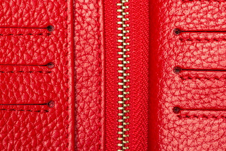 Close-up of red leather wallet texture with metal zipper and card slots, detailed surface for fashion, craft, or design concepts.の写真素材