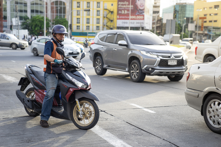 a delivery motorbike taxi man is ridding a motor cycle on busy street in city. Bangkok, Thailand.のeditorial素材