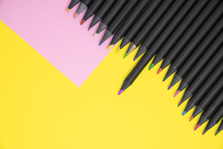The top views of black color pencils colored in shades of pink and yellow on colour paper background with copy space.の写真素材
