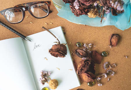 top view flat layer witerd old rusty brown roses and love word  on blank white book with blurry...