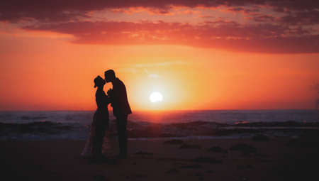 silhouette of couple lovers, bride and groom holding hands during sunrise time at the beach with beautiful pink sunrise sky.の写真素材