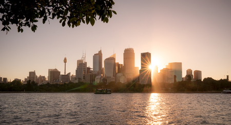 View of Building in Sydney City, during sunset time in Summer hot day, The sun is bright behind, and a ferry cruises on harbour in front of buildings.のeditorial素材