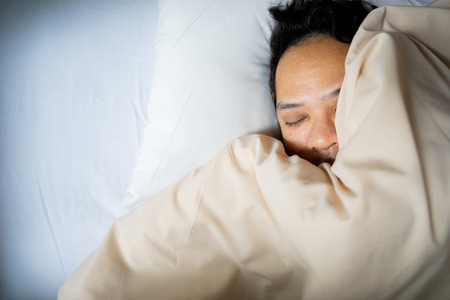 close up of an Asian man face sleeping on white bed, top view