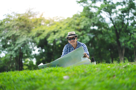 A happy traveller senior man sit in Forrest, opening a mapの写真素材