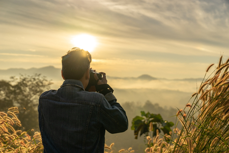 half length a Caucasian man taking photo of foggy mountain in sunrise timeの写真素材