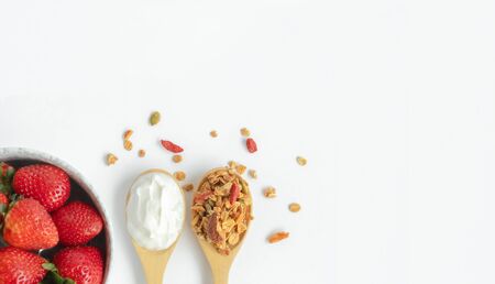 top view granola and yogurt in wooden spoons on white background with fresh strawberry in white ceramicbowl, idea for banner with copy spaceの写真素材