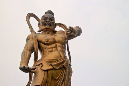 Bronze statue of a Chinese warrior deity against the hazy skyの写真素材
