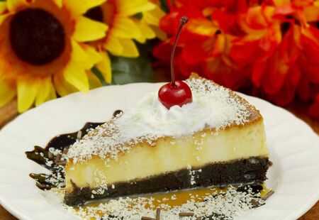 Chocolate cake based Flan with fudge, white chocolate powder, whipped cream and a cherry. 100mm macro lens. Flowery out of focus background.の写真素材
