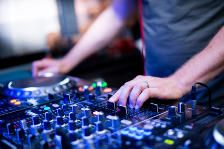 Party people Dj playing music on the turntable with the hands on the mixer console. The party is...