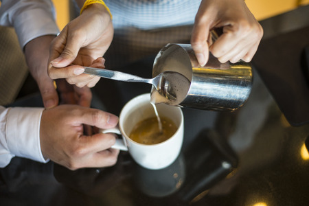 Waitress hands pouring milk making cappuccinoの写真素材