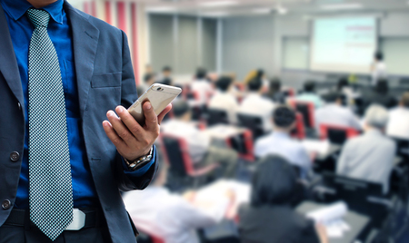 businessman using the mobile phone, blurred of conference hall or seminar room with attendee background.の写真素材