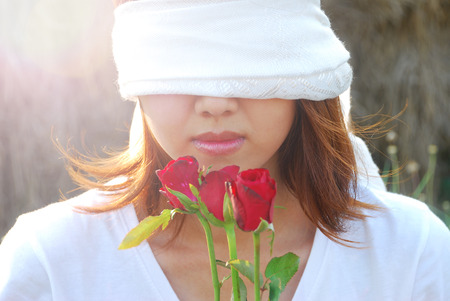 Asian young woman are bind with white scarf on her eyes in the light and flare in sunshine evening. In concept love is blind.の写真素材
