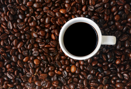 a white cup of black coffee lay on a lot of roasted coffee beans background
