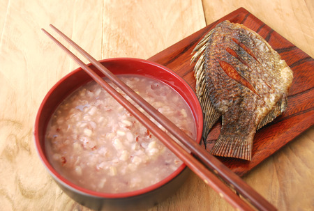 Boiled brown rice in a bowl with chopsticks and salty fish fried put in a wooden dish. Asians prefer to eat for breakfast.の写真素材