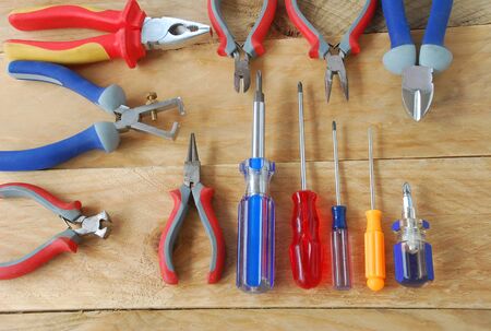 Tools, including pliers and screwdrivers in various sizes, colors such as blue, red, yellow, placed on a wooden floor in top view.の写真素材