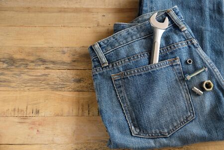 blue jeans have a metalic wrench in back pocket and bolts decorated on the wooden backgroundの写真素材