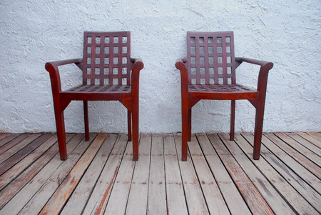 A couple old brown wooden chairs decorated on the old wooden floor with rough white wall.の写真素材