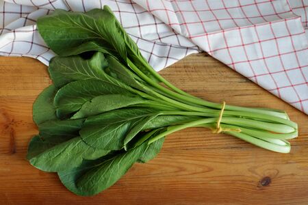 Fresh cantonese vegetables tied into a bundle, placed on a brown wooden plate and decorated with hand towels. Cantonese are vegetables that Asian people use to cook in soups or noodles.の写真素材