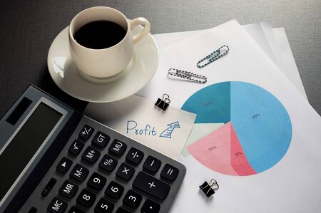 The office desk has written message Profit in blue ink on white paper,  has a circle graph in the...