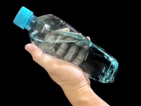 Hand holding a clear plastic bottle of pure drinking water refreshing on black backgroundの写真素材