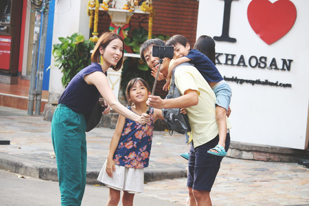 BANGKOK, THAILANS- JUNE 3 2018 : Father carrying his son on back taking picture with his family by smartphone on selfie stick and hiking at Khao San Road ,Bangkok ,Thailand.のeditorial素材