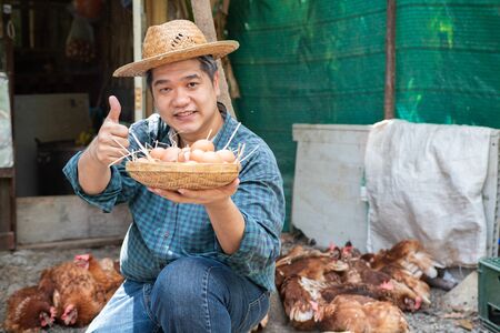 Proud eldery man holding a basket filled with eggs with chickens behind himの写真素材